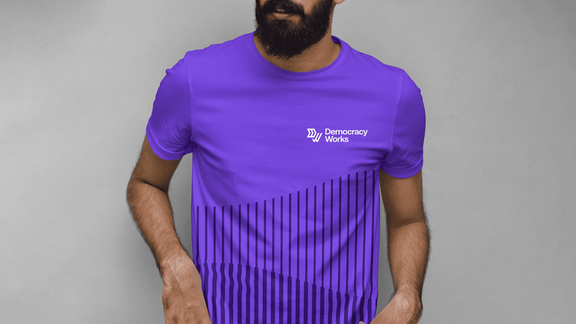 A man wearing a purple Democracy Works t-shirt with the logo on the chest and a vertical stripe pattern